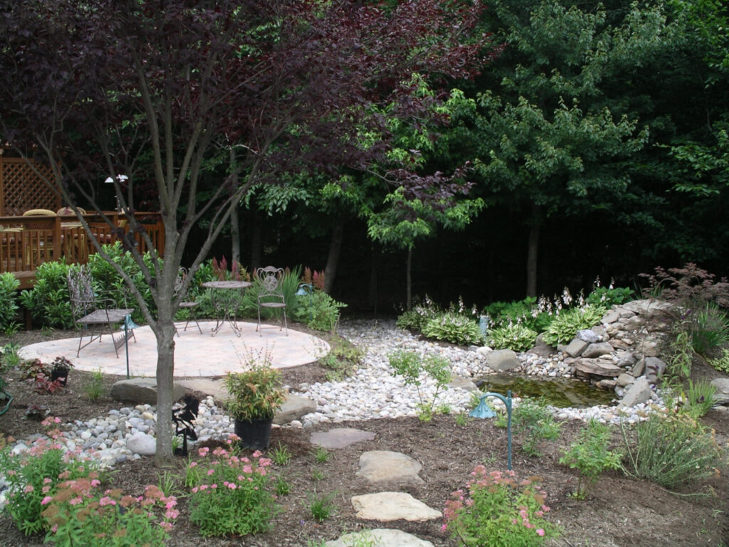 Yard with Stone Patio Surrounded by Gravel and Grass with Trees Overhead